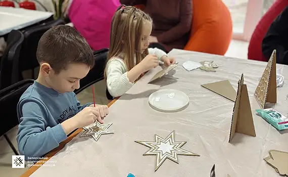 Діти розмальовують імпровізовані різдвяні прянички разом зі студентами коледжу